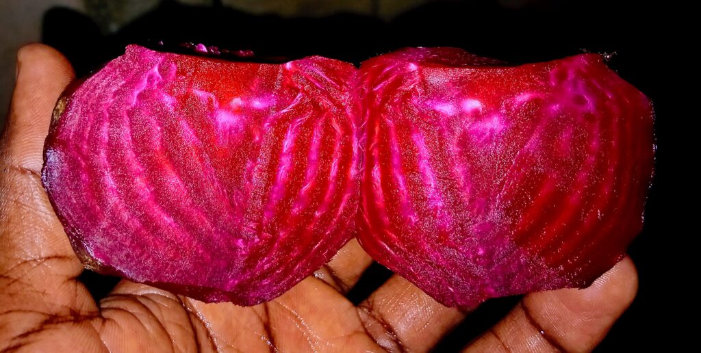 A close-up of a beetroot split into two halves, revealing its vibrant purple-red interior against a white background.