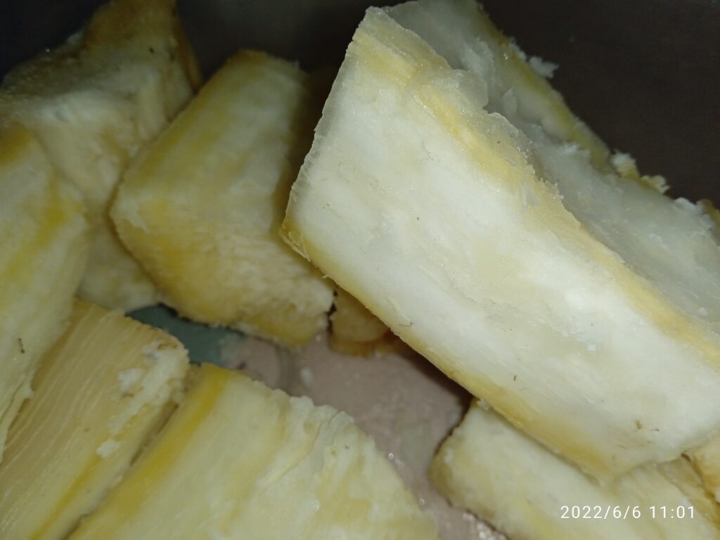 A close-up of whole cassava nuts scattered on a textured wooden surface, showcasing their brown, elongated, and slightly wrinkled appearance.