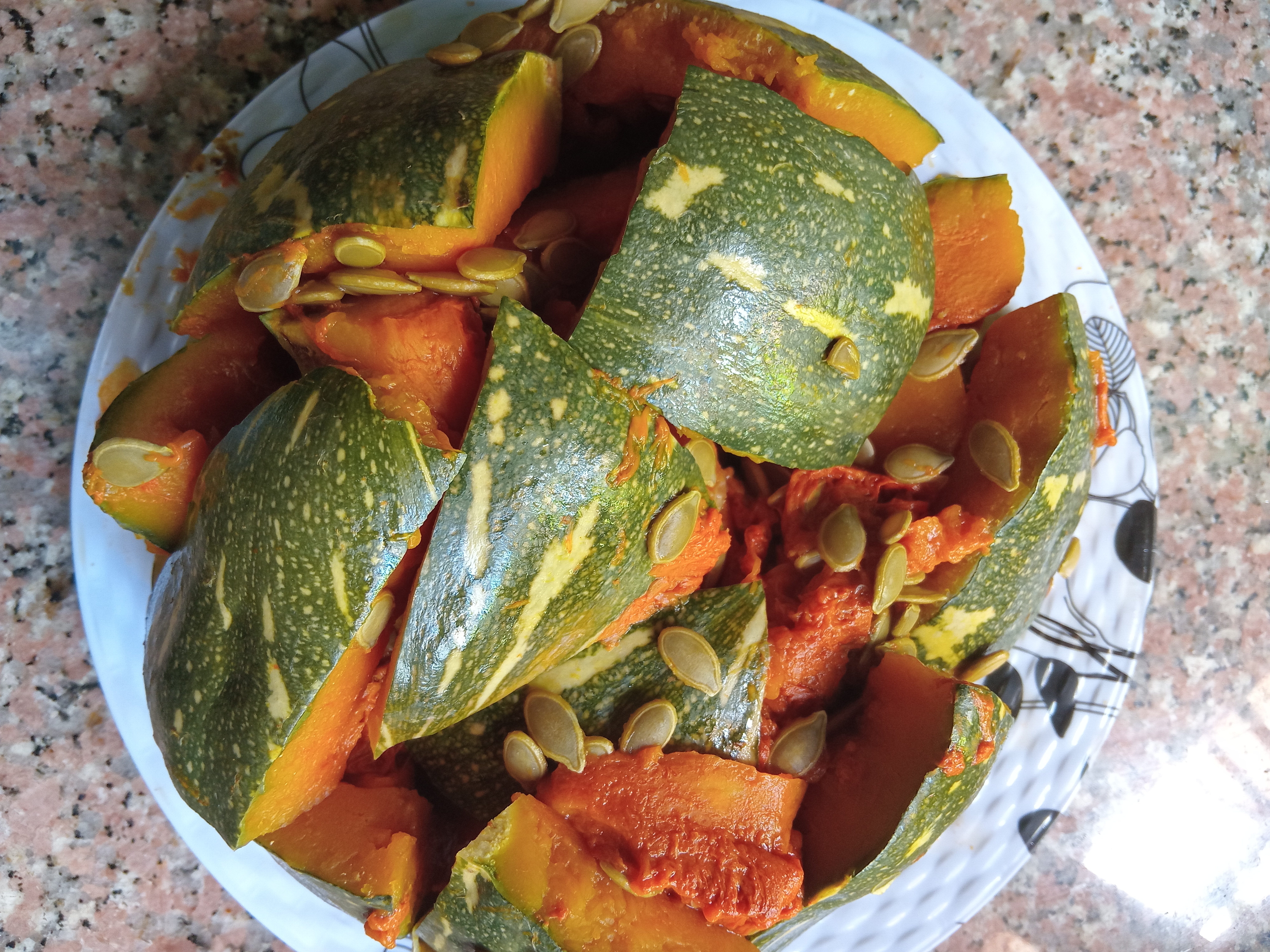 A cooked pumpkin, halved and roasted, placed on a white plate with a rustic wooden table in the background.
